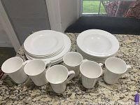 Set of white Mikasa dinnerware including 6 dinner plates, 5 shallow bowls, and 6 mugs arranged on countertop.
