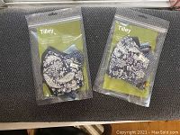 Two sealed packages of Tilley brand face masks showing multiple patterned masks inside packages.