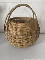 Full view of the woven basket showing rounded shape and sturdy handle wrapped in woven material.