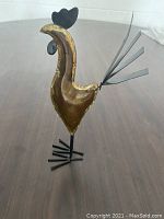 Metal rooster standing upright with visible golden brown and black metal parts, showing its side profile.