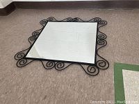 Full view of the square mirrored surface on floor with visible black curled metal frame edges