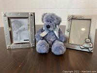 Lot showing both baby-themed picture frames and blue-gray plush teddy bear placed on a table