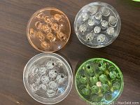 Top-down view of four round glass flower holders in green, pink, and clear glass, showing multiple holes in each for flower arrangement.