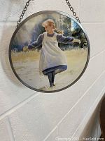 Full view of circular stained glass hanging piece depicting Anne of Green Gables, a girl in a blue dress and white pinafore.