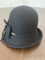Black rounded crown hat with a narrow brim and decorative bow detail on the right side.