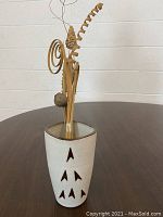 Cream-colored ceramic vase with triangular cut-outs, holding a variety of natural dried decorative picks including spirals, curls, and fan shapes.