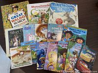 Photo showing the lot of 14 children's books arranged on a wooden surface, including titles: The Great Waldo Search, Rabbit's Winter Walk, and others.