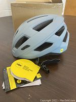 Side view of the light gray bike helmet showing ventilation slots and attached tags.