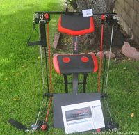 Front view of the Nano Gym Supreme portable home gym on grass showing padded swivel seat, arm resistance bands, and manual.