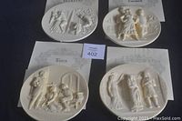 Four ivory alabaster plates featuring bas-relief scenes from operas Carmen, Rigoletto, Tosca, and Aida.