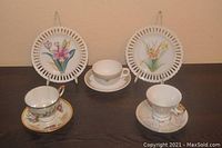 Lot content showing three tea cups and saucers along with two dessert plates, arranged on a table.