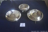 Set of three silver plated serving dishes on black cloth showing two covered casseroles and one compote dish
