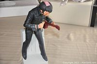 Side view of Elvis Presley figurine decanter in black outfit, seated on white box base, holding guitar with pink accents on hair and instrument.