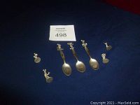 Photo showing all three Disney-themed pewter teaspoons and four small pewter game pieces on a dark fabric background.
