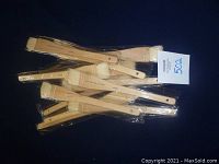 Set of 12 individual wooden-handle flat artist brushes in plastic sleeves shown grouped together on dark background.