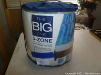 Packaged mattress topper in a blue cylindrical bag showing brand and product details.