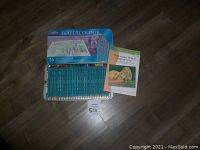 Full kit showing 36 watercolor pencils in blue metal tin, box cover and instruction book placed next to it on floor.