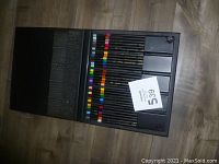 Open black carrying case showing rows of colored pencils with black barrels and colored ends, arranged in a foam insert inside the case