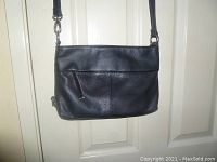 Front view of Tignanello black pebbled leather crossbody organizer bag hanging against a door showing the front zip pocket and part of the strap.