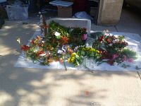 Multiple bunches of varied silk and artificial flowers and greenery spread out on white sheet with large plastic tote behind.
