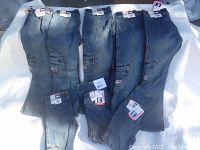 Eight pairs of blue denim girls jeans neatly laid out with tags visible, showing cargo pockets and L.E.I. branding.