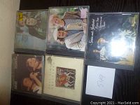 Five Simon and Garfunkel CD cases displayed on dark wood surface showing album covers with artists and titles, including one with Paul Simon solo.