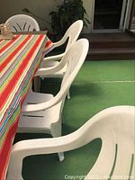 Photo showing four white plastic outdoor chairs arranged around a table with a colorful striped tablecloth.