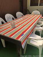 Full view of outdoor wood table covered with colorful striped tablecloth, surrounded by white plastic chairs