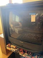 Front view of large black Panasonic CRT television showing reflective glass screen, set in home environment with furniture reflected.