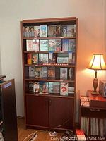Front view of the tall wood bookshelf filled with books and DVDs. Shows overall structure and condition of shelves and cabinet doors.