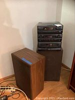 Stereo system and two speakers positioned in a corner, showing wood finish side panels on speakers and stacked black stereo components.