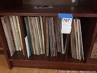 Photo of wooden shelf with multiple vinyl records stored vertically, showing titles and album covers on the spines.