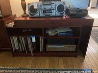 Front view of wooden table and cabinet showing stereo boombox, turntable, stereo receiver, and lamp on top and in shelves