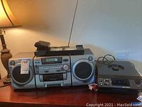 Aiwa boom box stereo system with cassette deck and radio tuner placed on a wooden table.