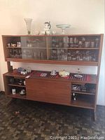 Wide shot of wooden cabinet containing various glassware and ceramic pieces including plates, cups, dishes