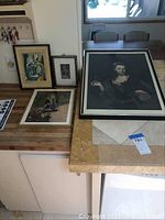 Six framed art prints laid out on kitchen counter and table showing portraits and people prints
