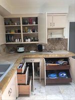 Kitchen cupboards with open doors showing stacked plates, cups, mugs, and some small containers and kitchen gadgets.