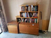 Full view of the bookshelf with books on shelves, cabinets below with one door broken on the right side.