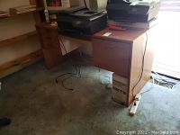 Full view of wooden computer desk with drawers, showing scratches and wear on surface, with printer and other office items on top.