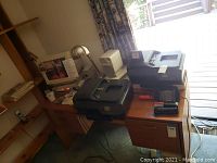 Wide shot showing two HP OfficeJet printers on a wooden desk, CRT monitor, keypad device, desk lamp, and various accessories around.