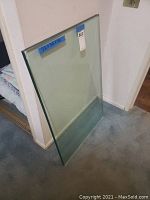 Glass table top standing against a wall on carpet floor, showing full rectangular shape and thickness.