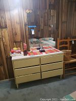 Full view of the chest with mirror in a room with wood-paneled walls and carpeted floor. Various items placed on chest top.