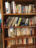 Three shelves of a wooden bookshelf packed with assorted wellness and general books, with small decorative items including figurines and candles interspersed among the books.