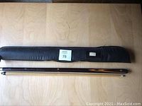 Black zippered carrying case with two-piece wooden pool cue laid out straight on wooden surface.