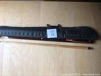 Full view of the pool cue disassembled into two pieces and black carrying case lying on a wooden floor.