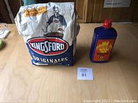 Photo shows partial 7.7 lb Kingsford Original charcoal bag and a Royal Oak charcoal lighter fluid bottle on a wooden surface.
