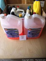 Two large translucent containers of red antifreeze/coolant in front of other fluid containers in a cardboard box.