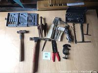 Overview of the lot showing hammer, puller tool, wrenches, multi-tool, clamps, wire stripper, and drill bit case on a wooden surface