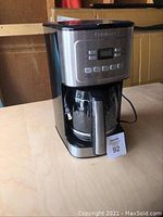 Front and side views of a black and stainless steel Cuisinart coffee maker with digital controls and glass carafe on a wooden surface.