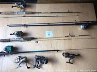 All four fishing rods laid out horizontally with reels attached and three spare reels aligned below them on a wooden surface.